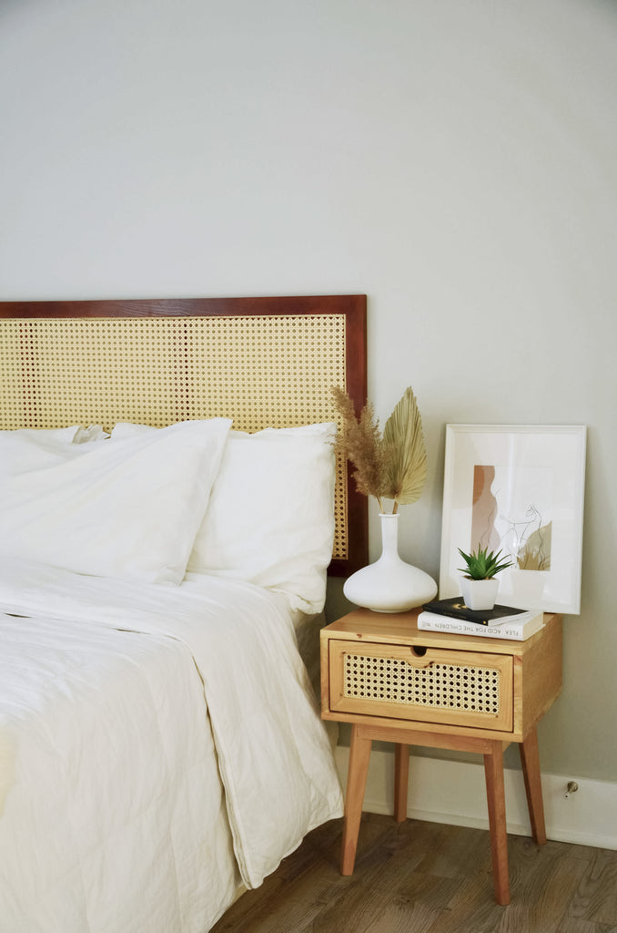 The bedroom looks vintage with a ash wood headboard and a simple side table. Both of that has a cane design.  